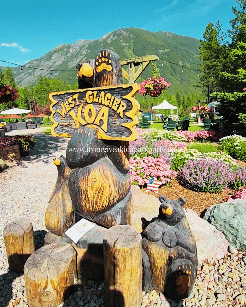 West Glacier KOA entrance with a bear and wooden sign featuring mountains in the background from Glacier NP.